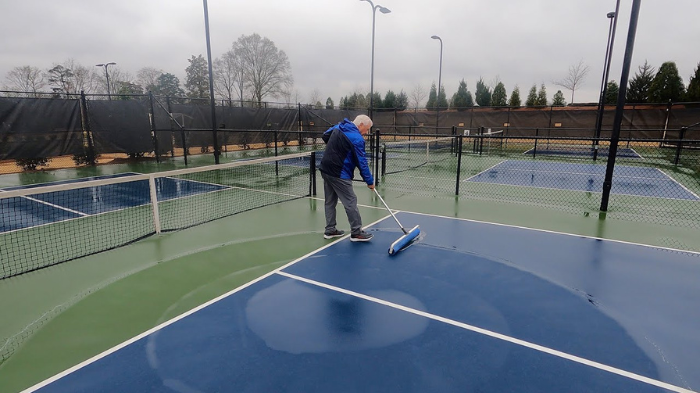 Pickleball Player Drying A Wet Pickleball Court Using Squeegee